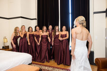 Load image into Gallery viewer, Bridesmaids in matching burgundy gowns laughing as the bride has her first look